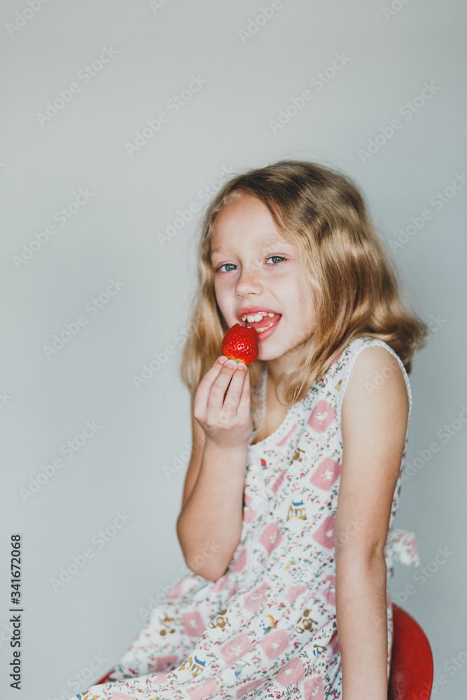 European blonde girl eating strawberries on a gray background. white teeth. healthy smile European blonde girl eating strawberries on a gray background. white teeth. healthy smile