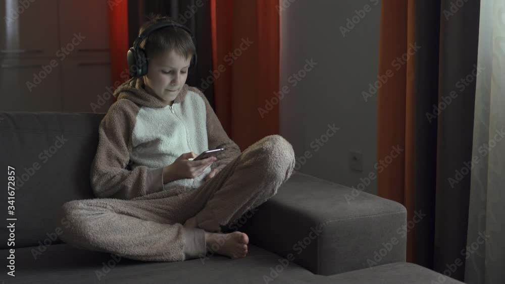 The guy in the headphones and with the smartphone in his hands sits on the couch listening to music. Quarantine 2020 The guy in the headphones and with the smartphone in his hands sits on the couch listening to music. Quarantine 2020