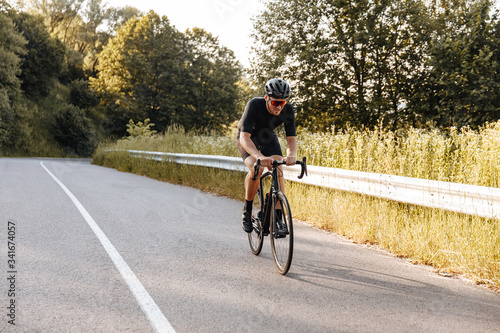Fototapeta Naklejka Na Ścianę i Meble -  Full length portrait of cyclist in sportswear dynamically riding bicycle during sunny days. Mature man in helmet and eyewear training on fresh air