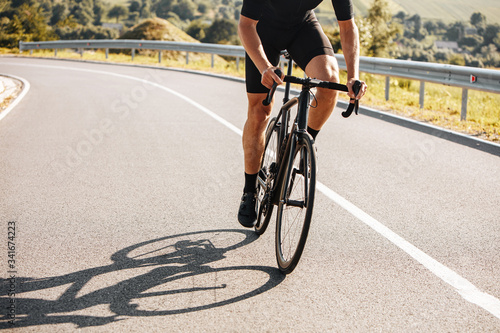 Close up of mature man with strong body wearing cycling clothing and sneakers, riding bike on countryside. Concept of active lifestyle and regular training. photo