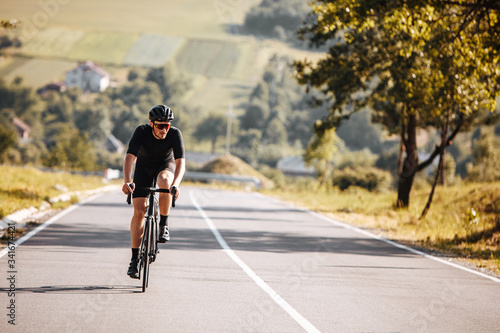 Fototapeta Naklejka Na Ścianę i Meble -  Front view of bearded man with athletic body shape in protective helmet and glasses riding bicycle with beautiful nature around. Concept of self discipline and motivation.