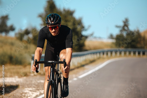 Fototapeta Naklejka Na Ścianę i Meble -  Front view of professional cyclist in sport outfit practising in cycling with blur background of green nature. Concept of summer activity and healthy lifestyle