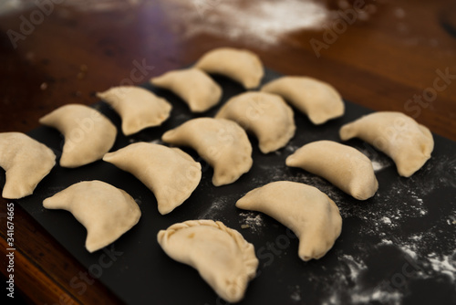 Uncooked russian vareniki on cutting wooden board with flour on baking paper. Process of making vareniki. top view.Typical Eastern European food, called dumplings, dumplings, dumplings, pies or pies