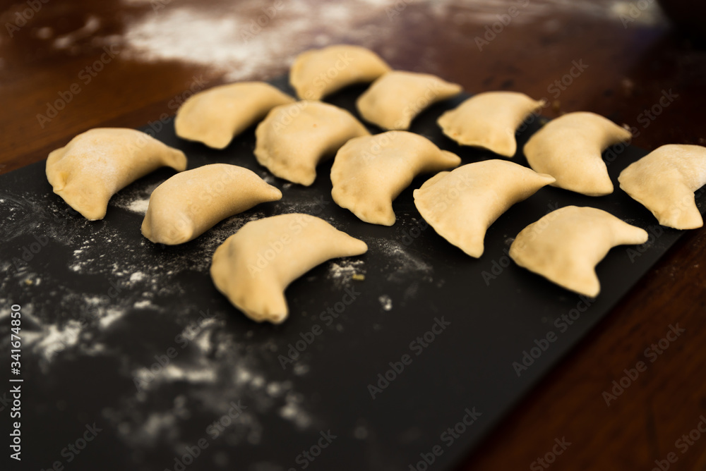 Uncooked russian vareniki on cutting wooden board with flour on baking paper. Process of making vareniki. top view.Typical Eastern European food, called dumplings, dumplings, dumplings, pies or pies Uncooked russian vareniki on cutting wooden board with flour on baking paper. Process of making vareniki. top view.Typical Eastern European food, called dumplings, dumplings, dumplings, pies or pies