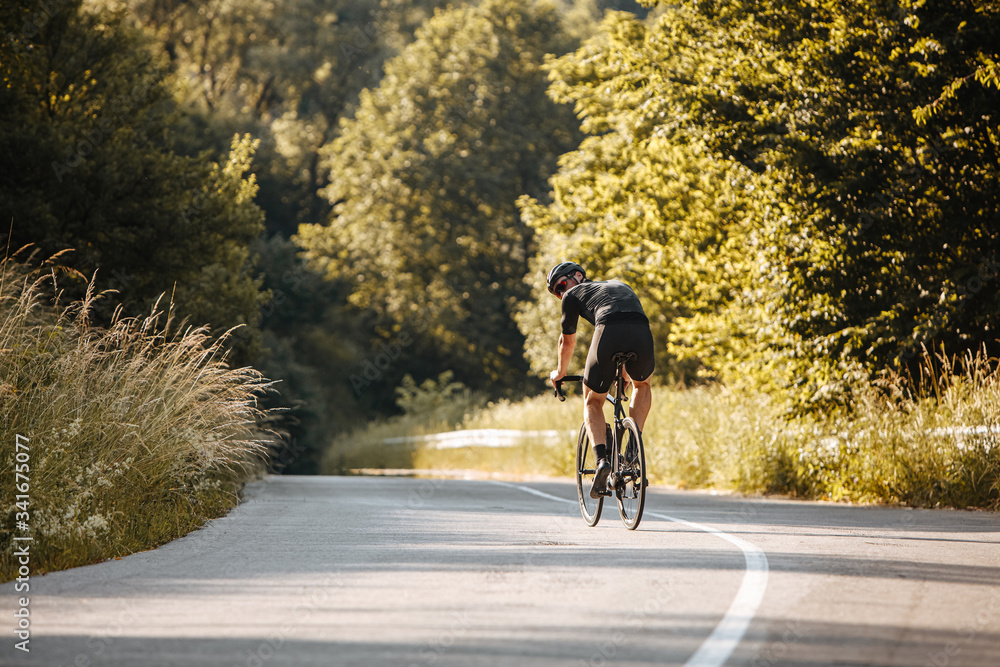 Active bearded man in sport outfit, black helmet and glasses biking among beautiful nature. Strong sportsman training regularly outdoors.