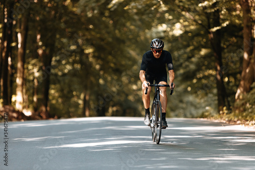 Active mature cyclist wearing black sport outfit, protective helmet and mirrored glasses riding in forest with blur background. Responsible sportsman training regularly outdoors. © Tymoshchuk