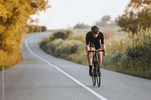 Professional male cyclist in black helmet, protective glasses and activewear dynamically riding bicycle on paved road with blur background. Concept of summer activity and healthy lifestyle photo