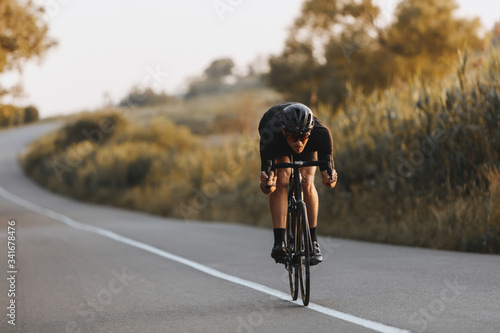 Professional sporty cyclist in black helmet, protective glasses and active wear dynamically riding bicycle in a half-bent pose for better speed. Man preparing for competitions and races on fresh air