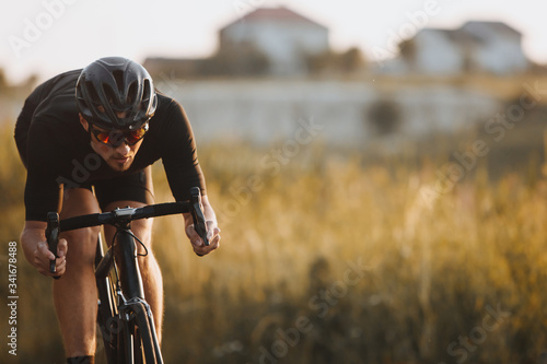 Close up of male athlete in cycling clothes, black helmet and protective glasses looks very concentrated while riding bicycle among nature countryside. Active lifestyle and sport concept