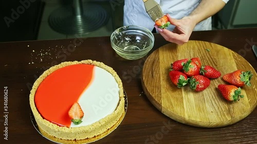 woman hands put by tassel glaze on half of fresh red strawberry above wooden tray