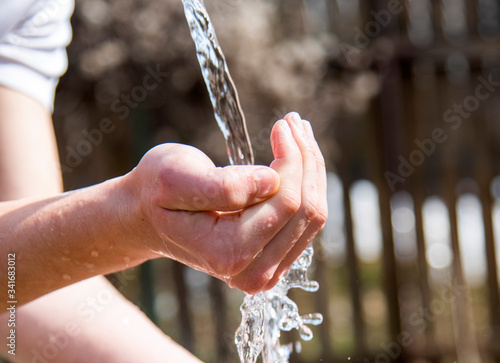 A young man's hand under a stream of clear water on a blurred background.