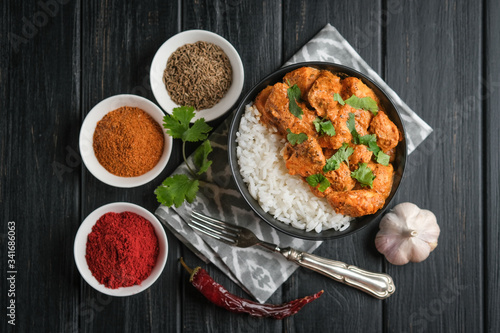 Chicken tikka masala traditional Asian spicy meat food with rice tomatoes and cilantro in a black bowl on dark background.