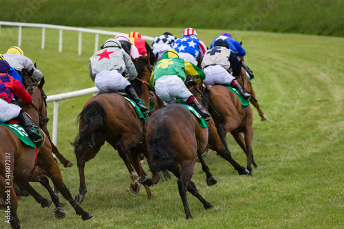 View from behing of race horses and jockeys galloping on the race track in the rian © Gabriel Cassan