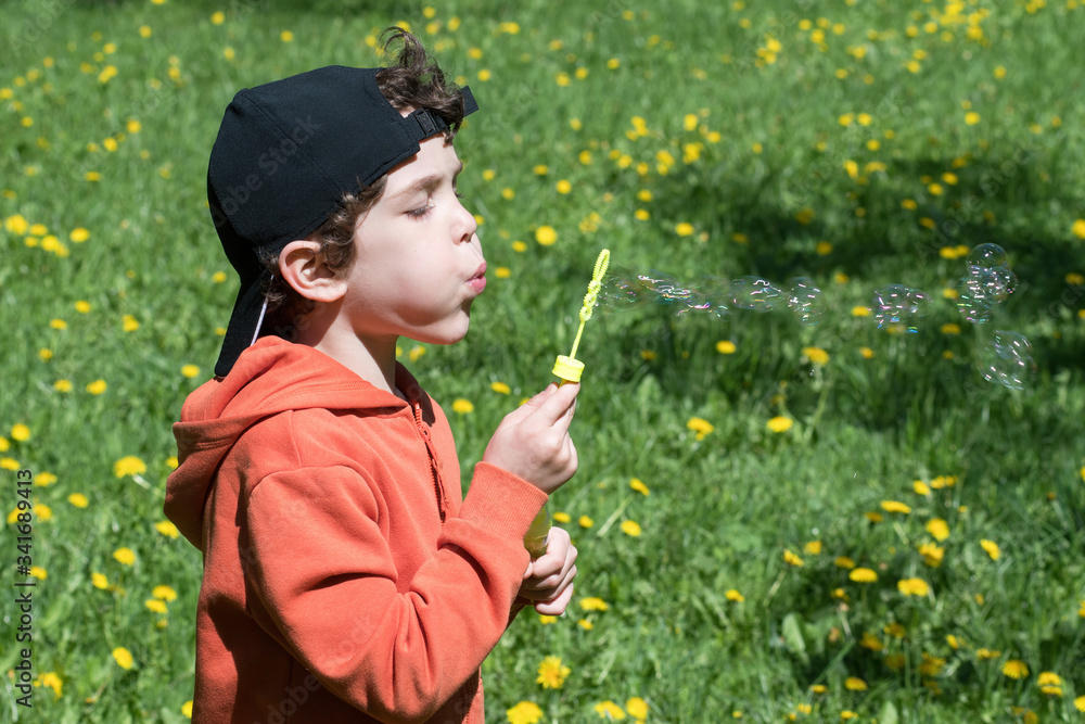 Six-year-old boy blows soap bubbles on the green lawn with blooming dandelions. Six-year-old boy blows soap bubbles on the green lawn with blooming dandelions.