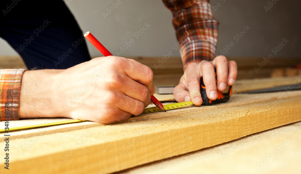The carpenter is measuring the length of the wooden board with tape-measure The carpenter is measuring the length of the wooden board with tape-measure