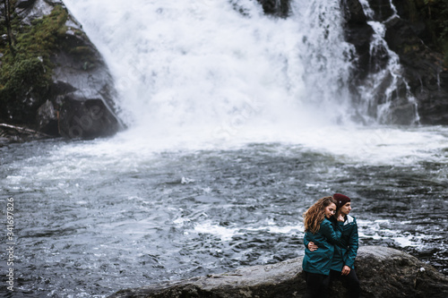 A couple of lovers in green raincoats, sitting on a rock, against the backdrop of a waterfall