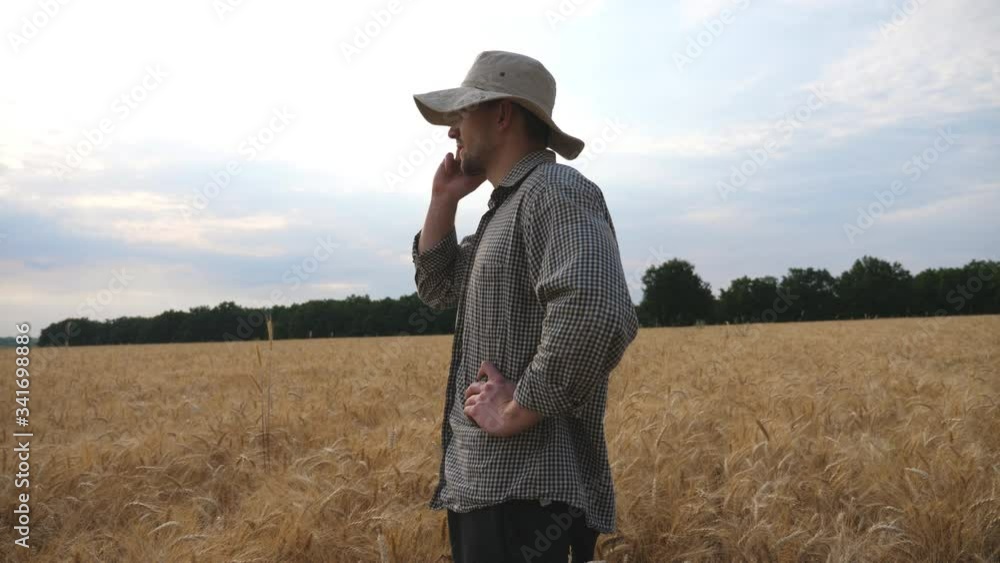 Close up of male farmer standing on the wheat field and talking on mobile phone. Young agronomist using cell phone for a business discussion on the barley meadow. Concept of agricultural business Close up of male farmer standing on the wheat field and talking on mobile phone. Young agronomist using cell phone for a business discussion on the barley meadow. Concept of agricultural business