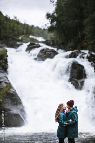 Portrait of lovers in green raincoats standing on the background of a waterfall