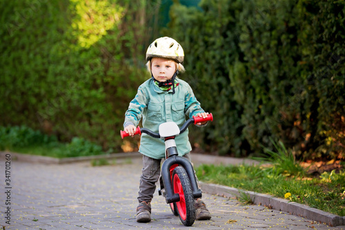 Fototapeta Naklejka Na Ścianę i Meble -  Blonde little toddler child in riding bike, wearing helmet and playing on the playground