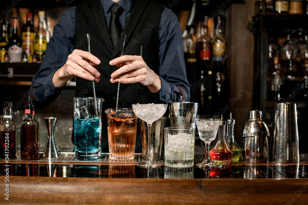 male bartender holds two spoons and mix cocktails with them