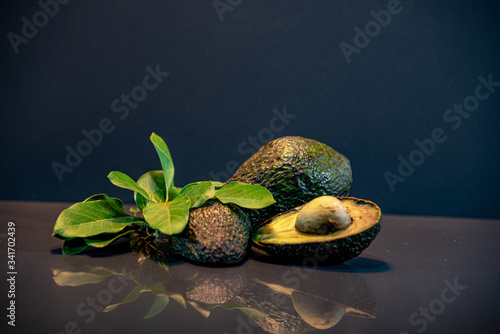 Fresh avocado fruit in halves with leaves and seed on dark background