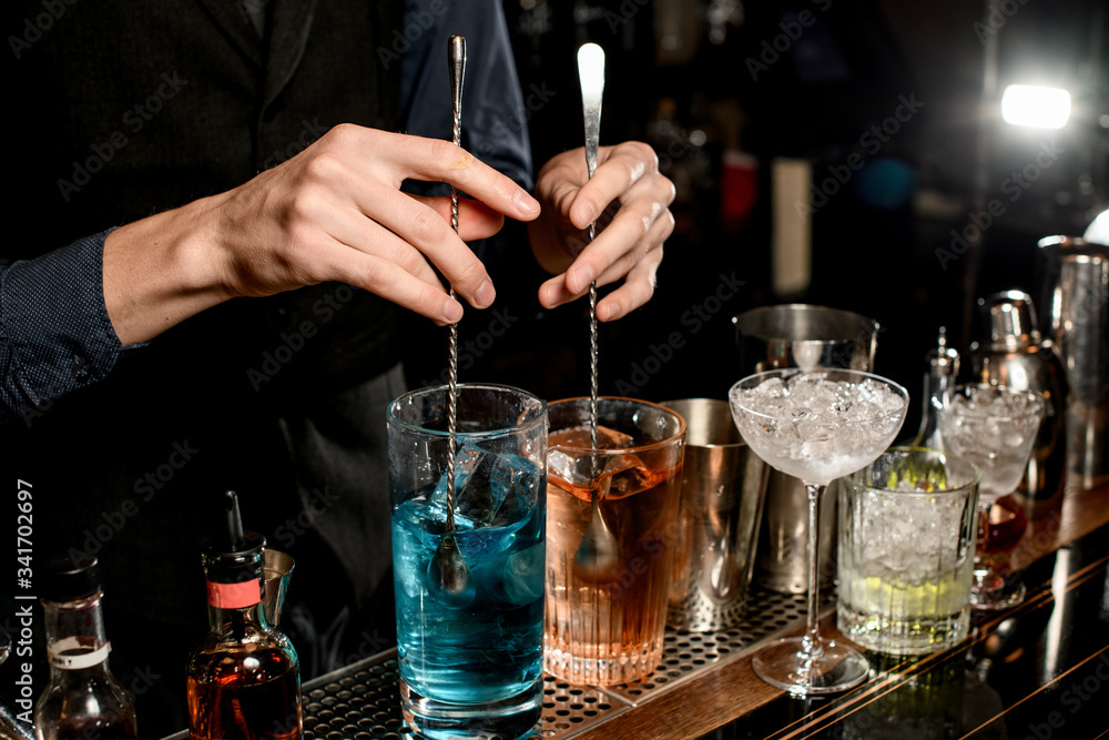 Close-up. Man bartender holds two spoons and mix cocktails with them