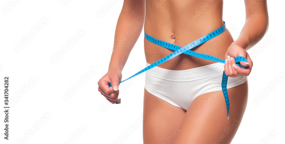 Weight loss - woman with trained belly. Young skinny female in white panties with tanned body is measuring her waist with blue tape measure and showing diet results. Studio shot, white background.
