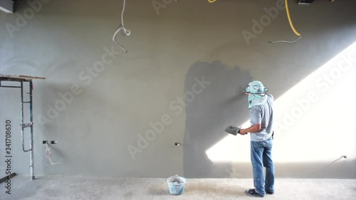 Back portrait workers plastering the cement on the concrete wall by trowel in the house under construction.