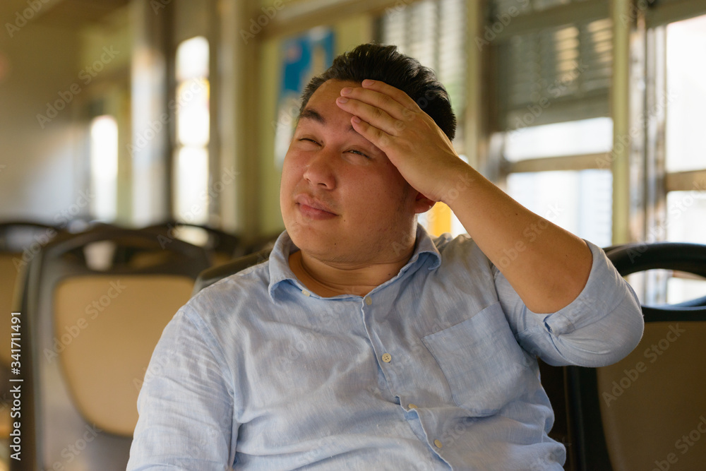 Obraz premium Stressed overweight Asian tourist man feeling hot inside the train