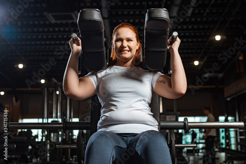 Photography cropped view of purposeful overweight girl doing arms extension exercise on fitn