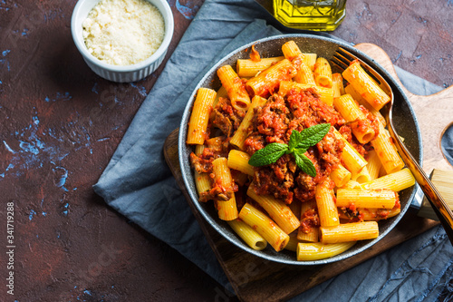 Delicious rigatoni pasta with italian tomato meat ragu sauce served in a pan on dark brown background. Traditional pasta dish concept. Home made lunch photo