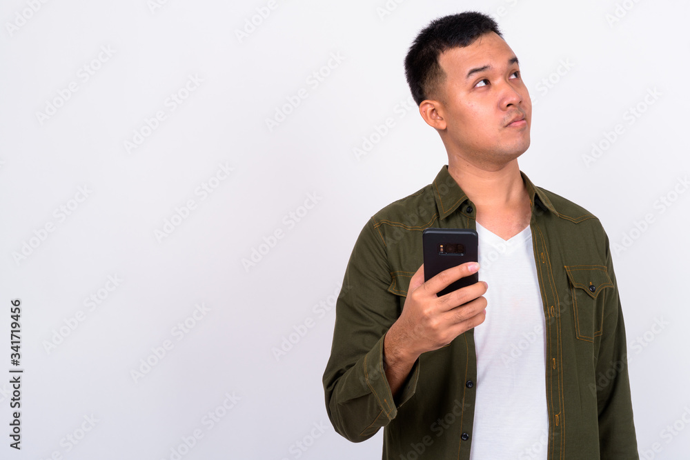 Portrait of young Asian man thinking while using phone Portrait of young Asian man thinking while using phone