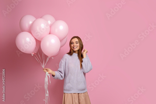 Smiling carefree girl posing with pastel pink air balloons isolated over pink background. Beautiful happy young woman on a birthday holiday. space for text