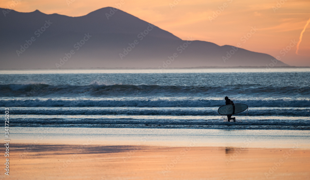 Silhouette of Surfer with surfboard coming out of the ocean at sunset, County Kerry on the west coast of Ireland