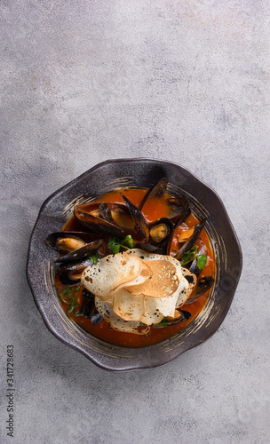 Seafood. Mussels in tomato sauce with herbs and croutons in a black plate on a light grey background. Top view, flatlay. Background image, copy space