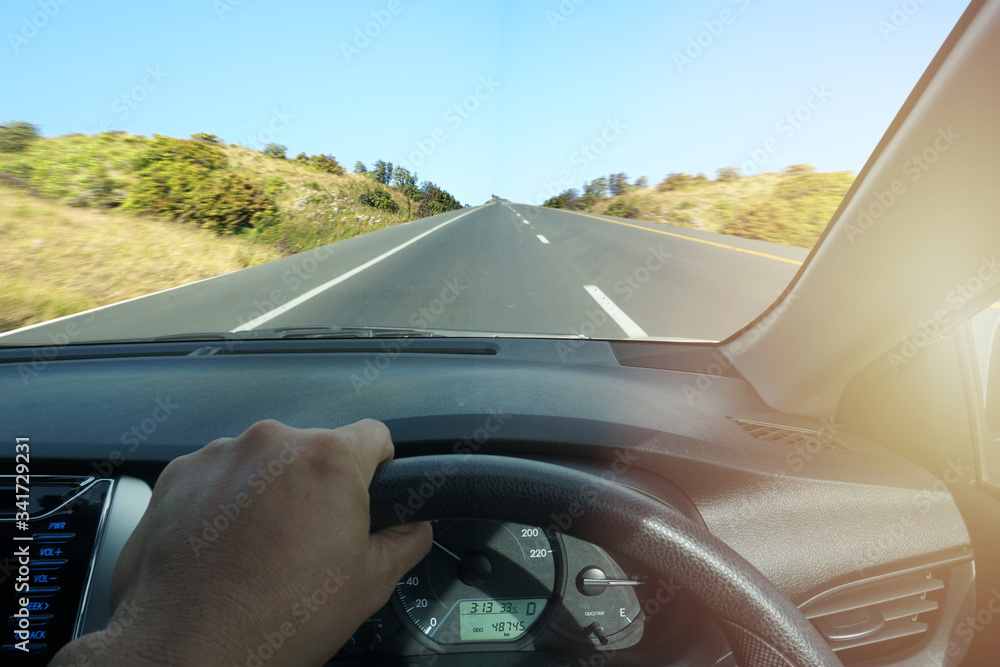 Close-up of the driver from the rear view on the highway, the maximum speed of not over 100 mph within the side view of the driver on the steering wheel of a car with an empty asphalt road.
