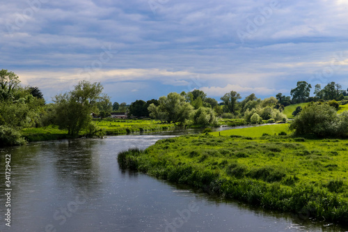 The dark waters of the River Boyne as it meanders through the Irish countryside in summer with lush green foliage along the banks of the river and an overcast cloudy sky above