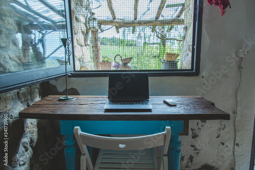 Home office desk made of recycled wood set up in a country house for smart working  with a view on the outside hills from the window. Quarantine and lockdown mood.