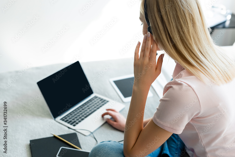 Naklejka premium selective focus of freelancer touching headset near laptop and digital tablet with blank screen on bed