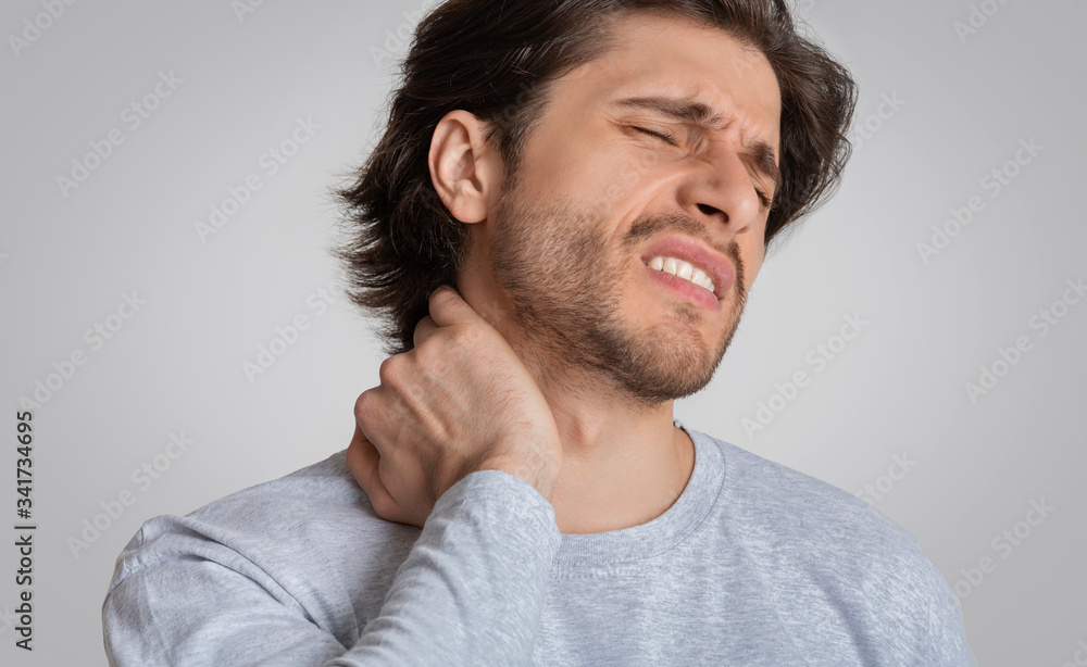 Man with painful expression rubs his neck Man with painful expression rubs his neck