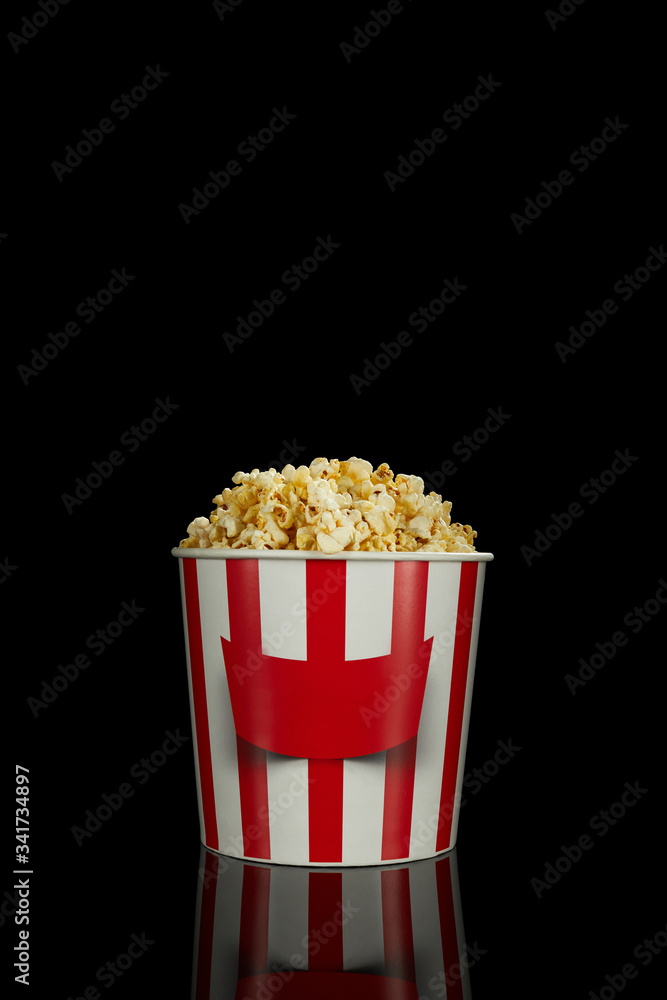 delicious fresh popcorn in classic red and white paper striped bucket isolated over the black background. delicious fresh popcorn in classic red and white paper striped bucket isolated over the black background.