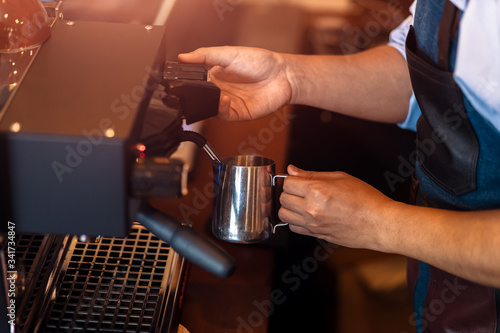 Barista steaming milk in the pitcher with coffee machine for preparing to make latte art.