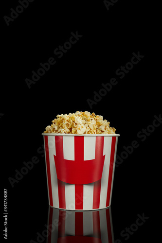delicious fresh popcorn in classic red and white paper striped bucket isolated over the black background.