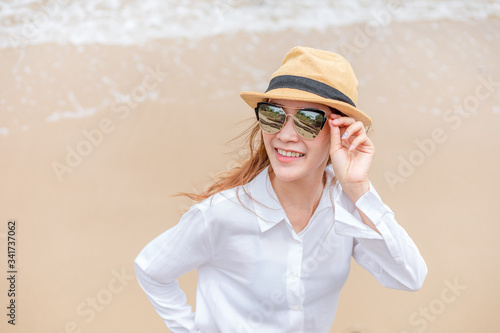 smiling young woman in sun hat and waring sun glasses on the  beach. summer, holidays, vacation, travel concept © Charnchai saeheng