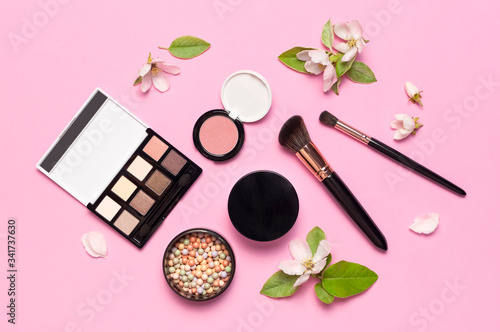 Decorative cosmetics mascara powder lipstick eyeshadow blush balls makeup brush perfume blooming spring branches on pink background top view Flat lay. Beauty blogger concept. Fashion background