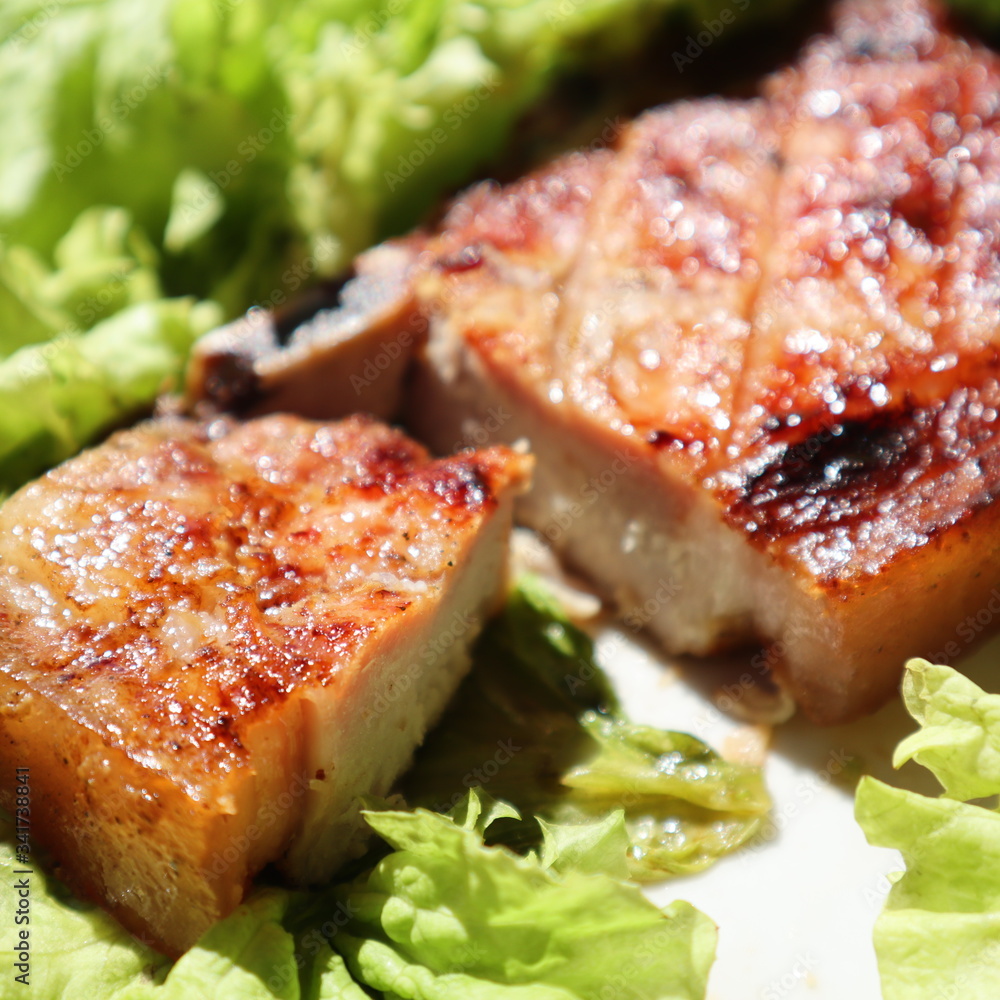 Juicy pork steak grilled on a plate on a fresh green salad