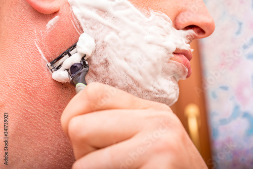 Close up of male shaving with razor. Man shaving his face with the razor blade through shave foam. Men skin care concept.