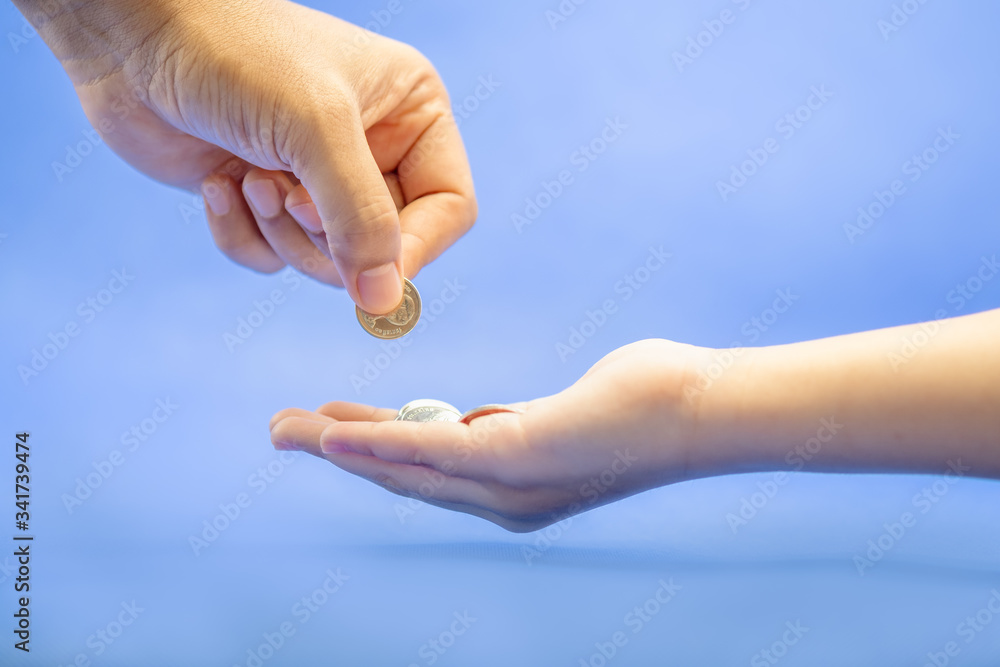 Closeup of father hand giviing coin to child hand on blue background with copy space for text. Closeup of father hand giviing coin to child hand on blue background with copy space for text.