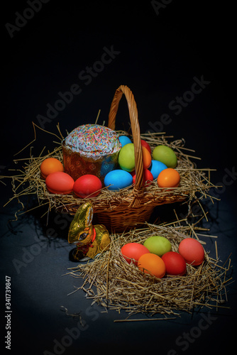 Easter colored eggs and Easter cake with straw in wicker basket on tblack background photo