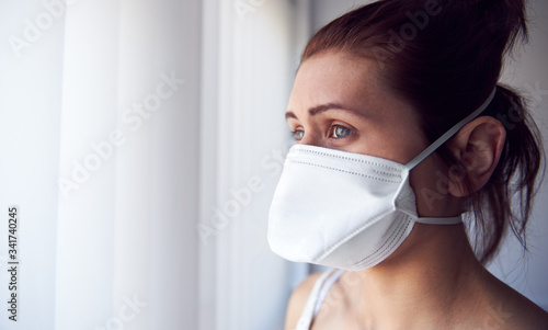 Young woman looking out of window wearing protective face mask.